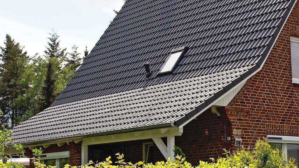 Toiture en tuiles sombres avec fenêtre de toit, au-dessus d’une façade en brique