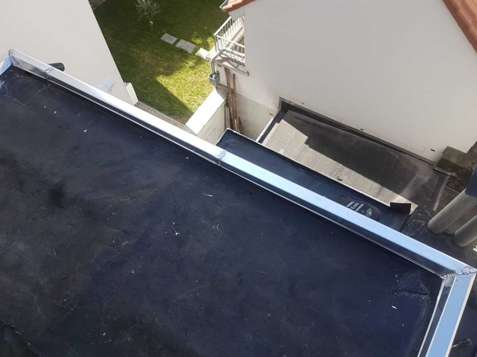 Toit plat revêtu d’une membrane sombre, bordé d’une rive métallique