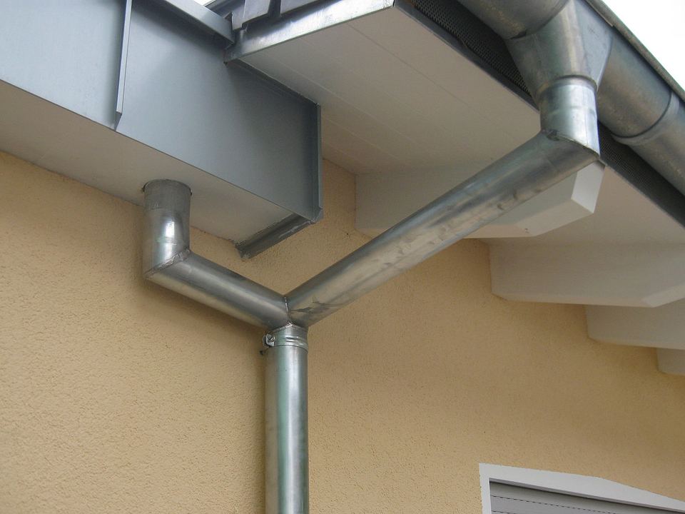 Gouttière et descentes en zinc fixées sous un débord de toit