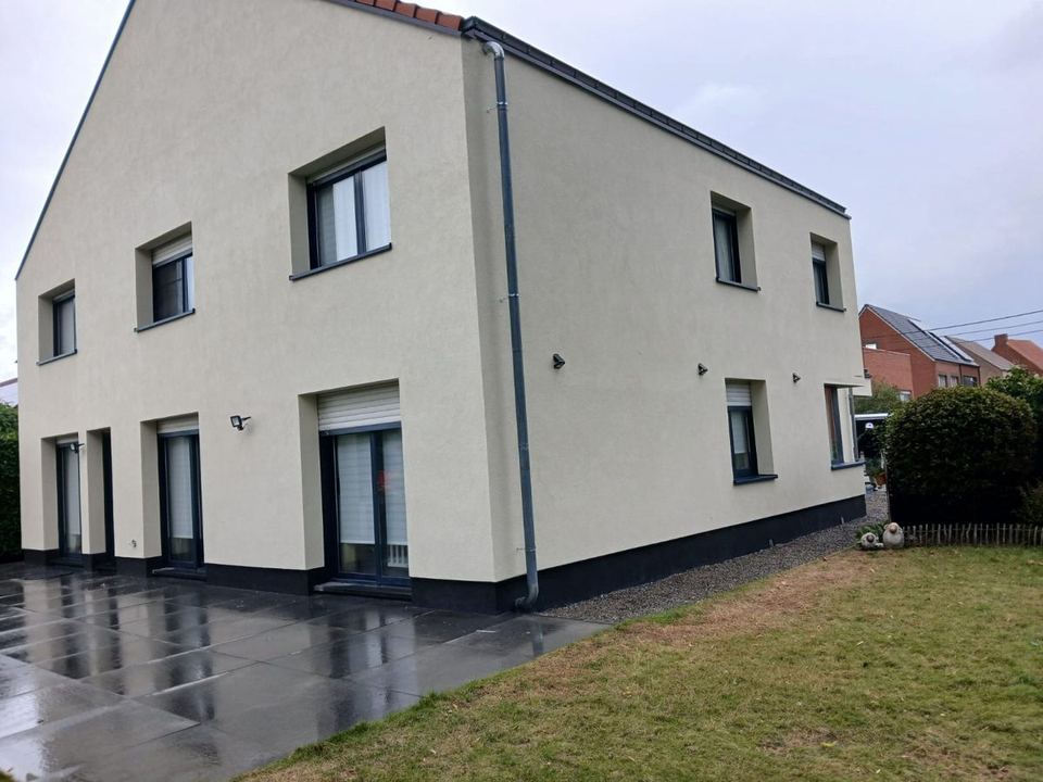 Maison individuelle à façade enduite claire, soubassement sombre et fenêtres alignées